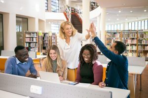 five adults smile around a library table with a laptop and two people high-five